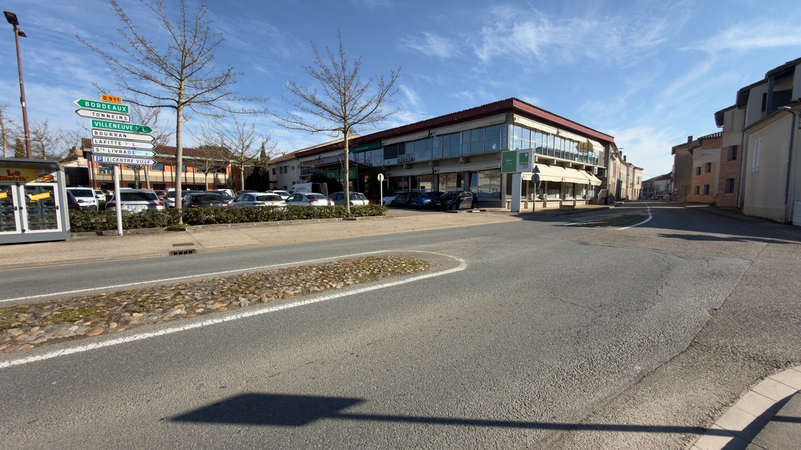 La place de Viau, l'herbe, la statue qui regarde la rue — le village en plein jour.